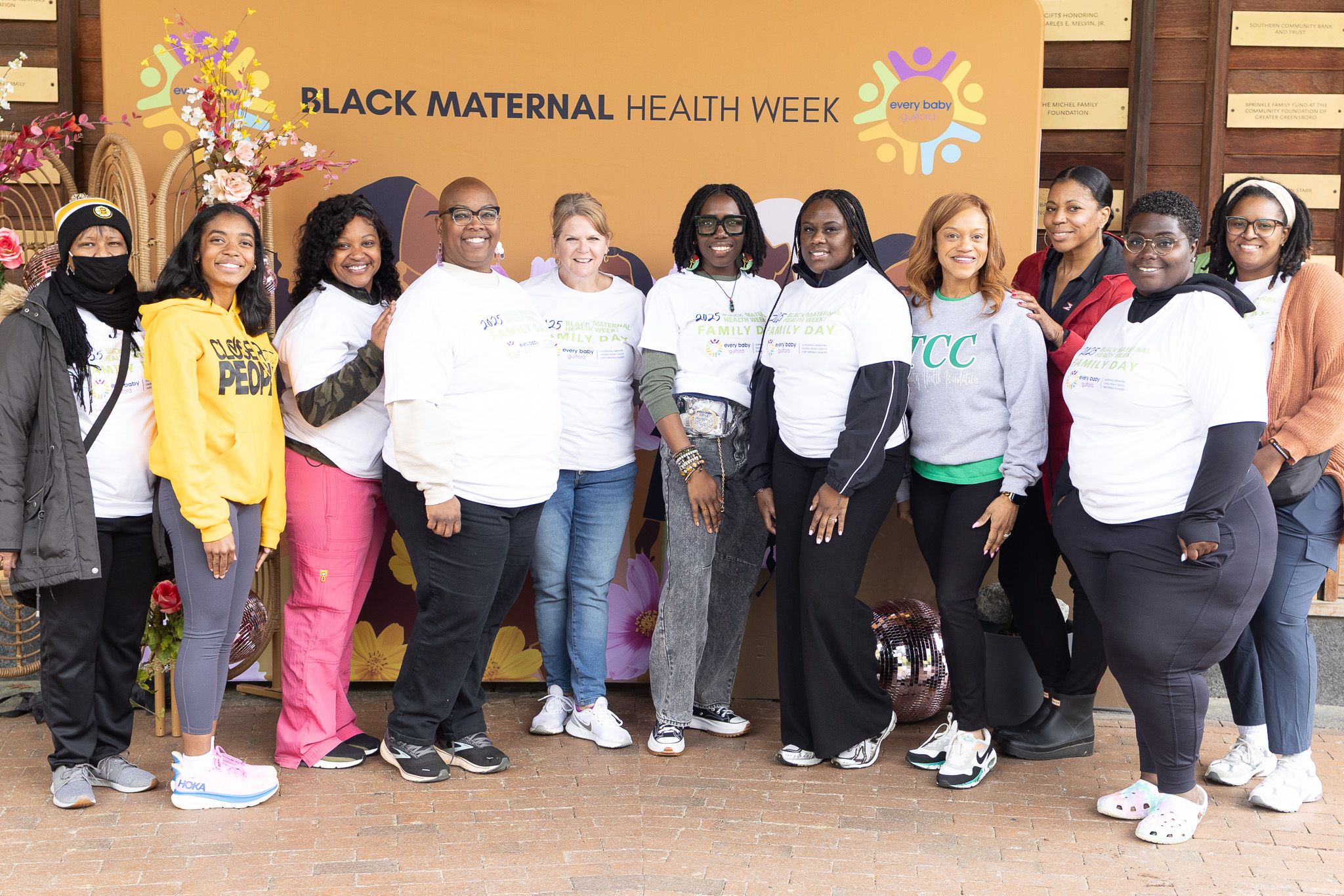 Diverse group of healthcare advocates pose together under Black Maternal Health Week banner.