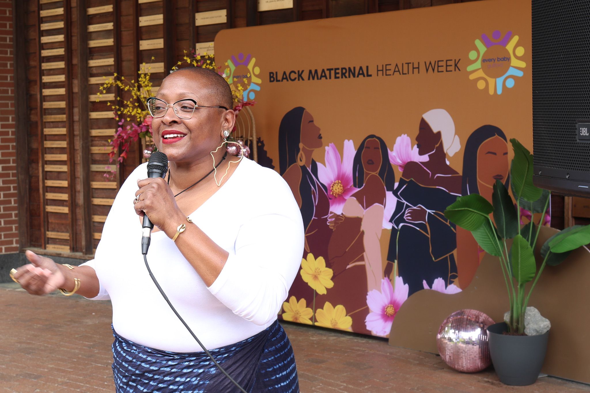 Speaker addresses audience at Black Maternal Health Week event with decorative backdrop.