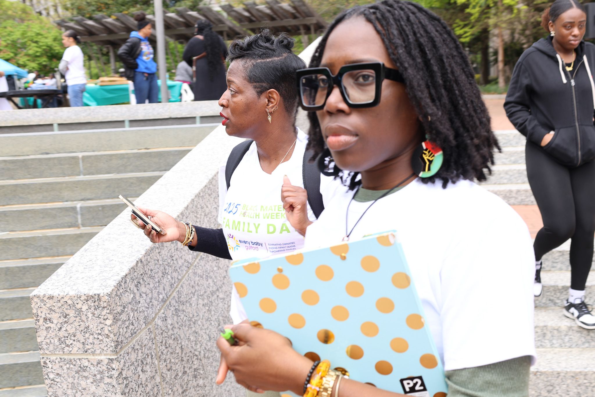 Attendees at outdoor community event carrying folders and materials.
