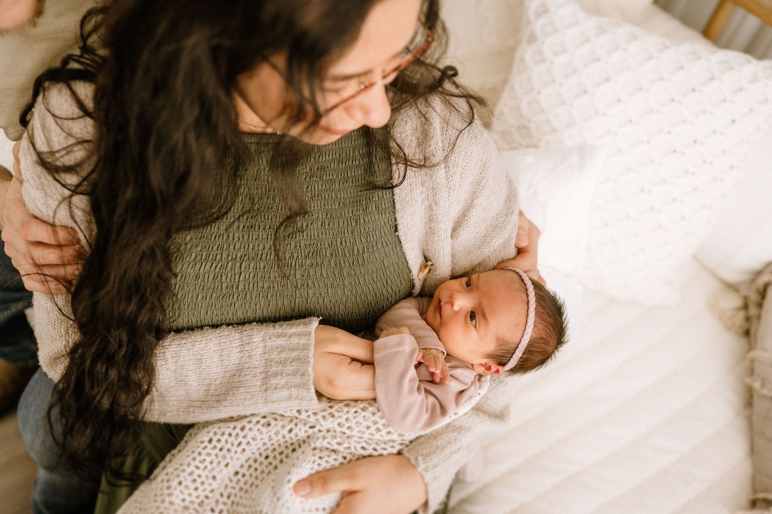 A smiling baby wearing a white knit dress lies comfortably on a white blanket while being cared for.
