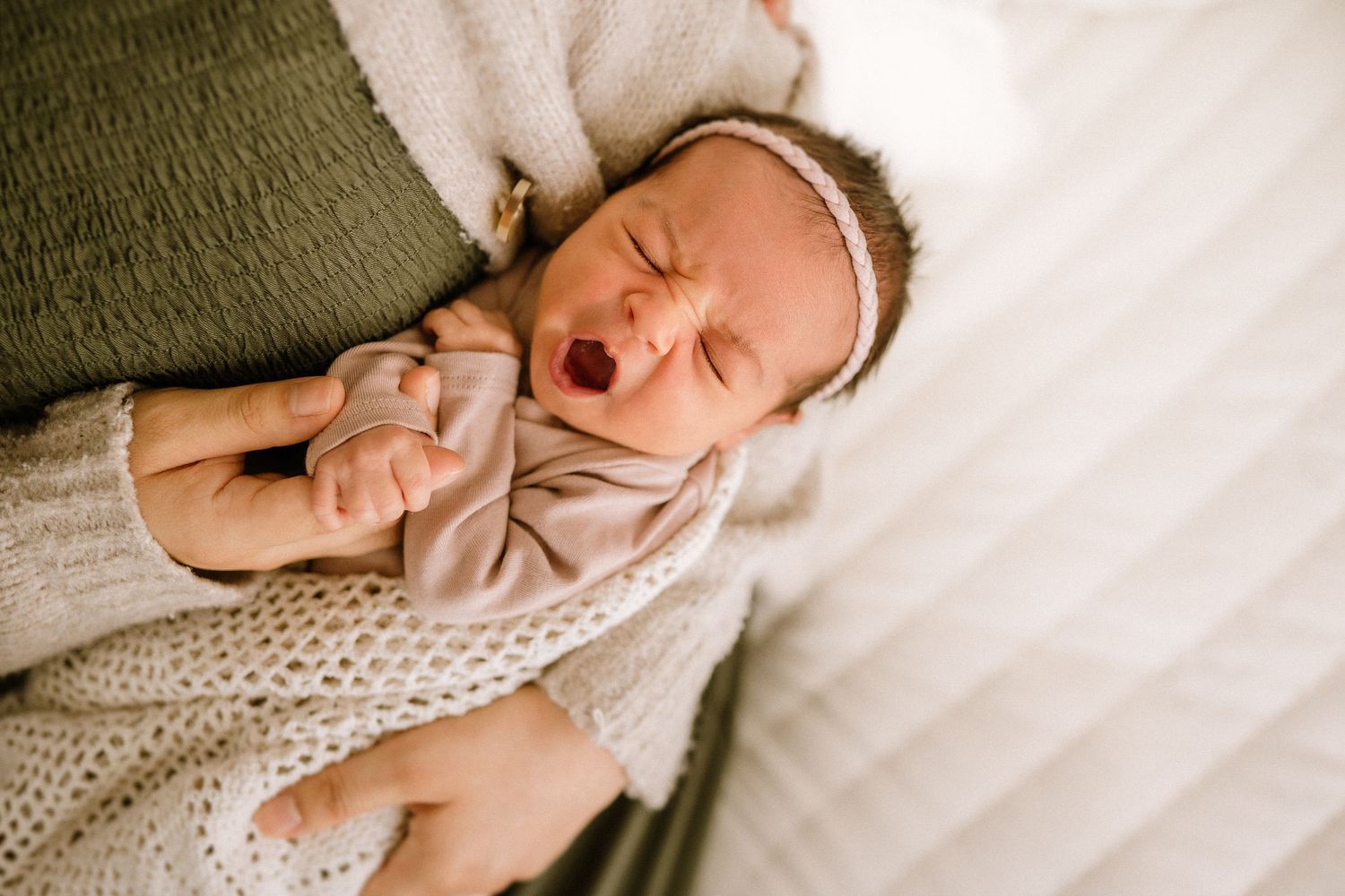 Newborn baby yawns while swaddled in cozy knit blanket during professional photo session.