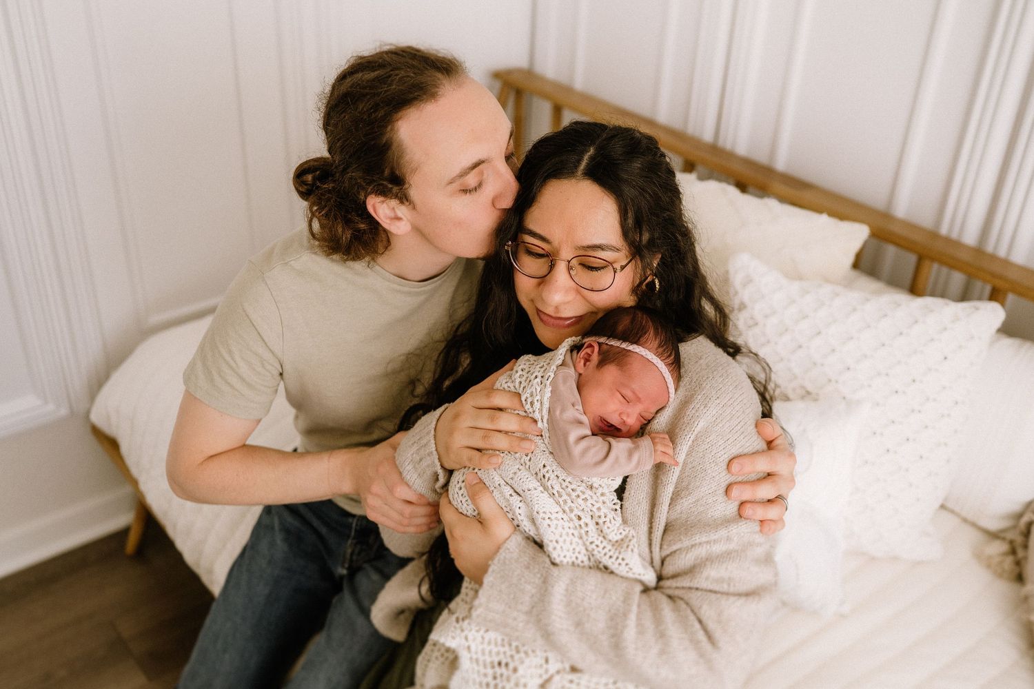 Intimate family moment showing parents snuggling with their newborn baby on a white bed.