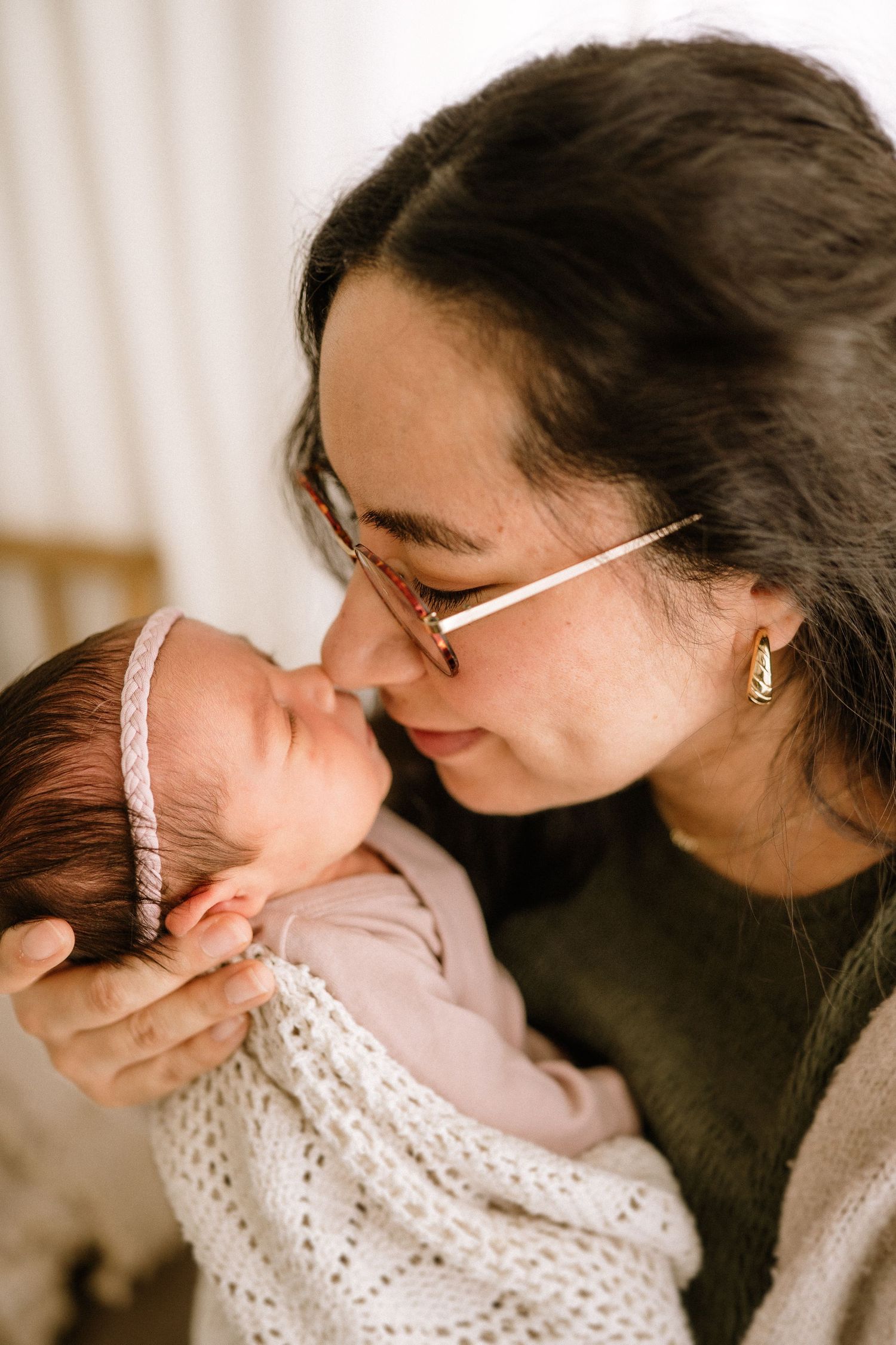 A tender moment captured of someone wearing glasses cradling and kissing an infant wrapped in a knitted blanket.