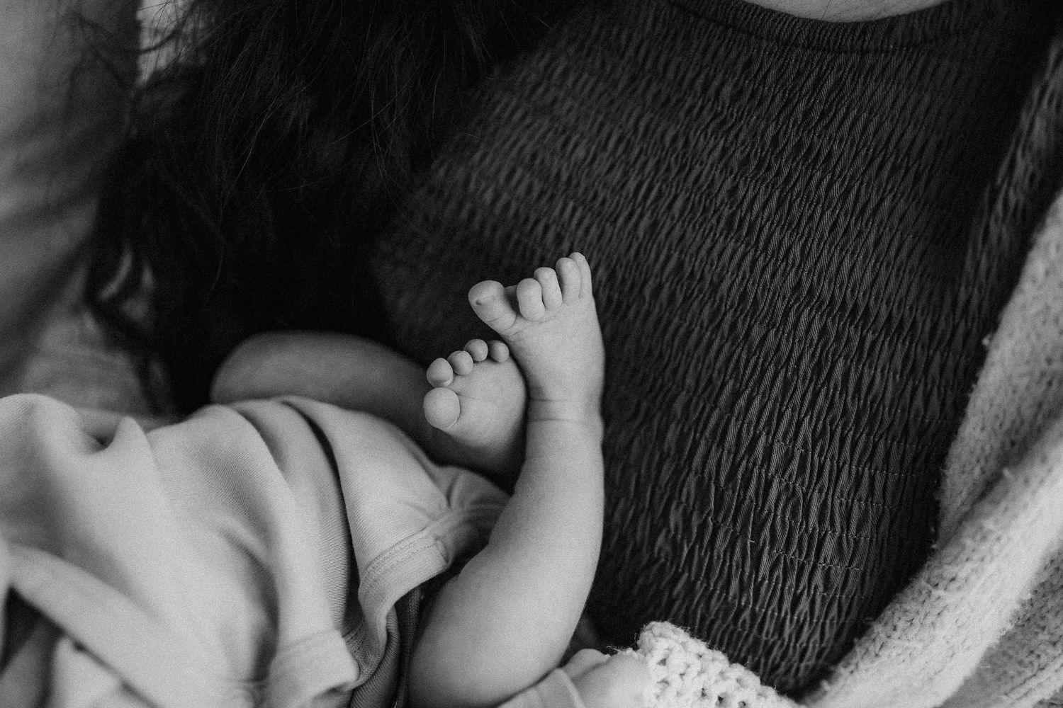 Black and white close-up photo of a small baby foot against textured fabric bedding.