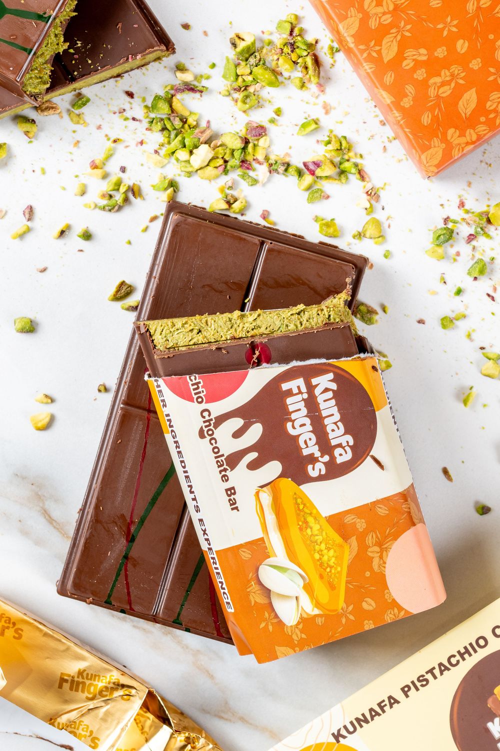 Artfully broken chocolate bars with pistachios and packaging displayed on white surface.