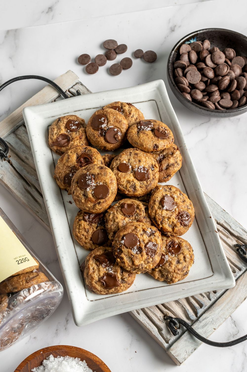Fresh baked chocolate chip cookies cooling on white marble counter with scattered chocolate chips.