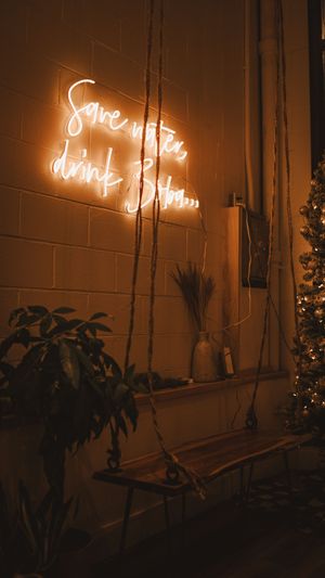 A warm glowing neon sign on a brick wall above a decorative swing and potted plants in a cozy evening setting.