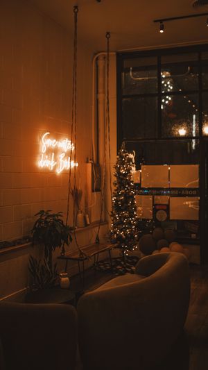 A cozy dimly lit room with a Christmas tree, neon sign, and plush armchairs creating a warm atmospheric ambiance.