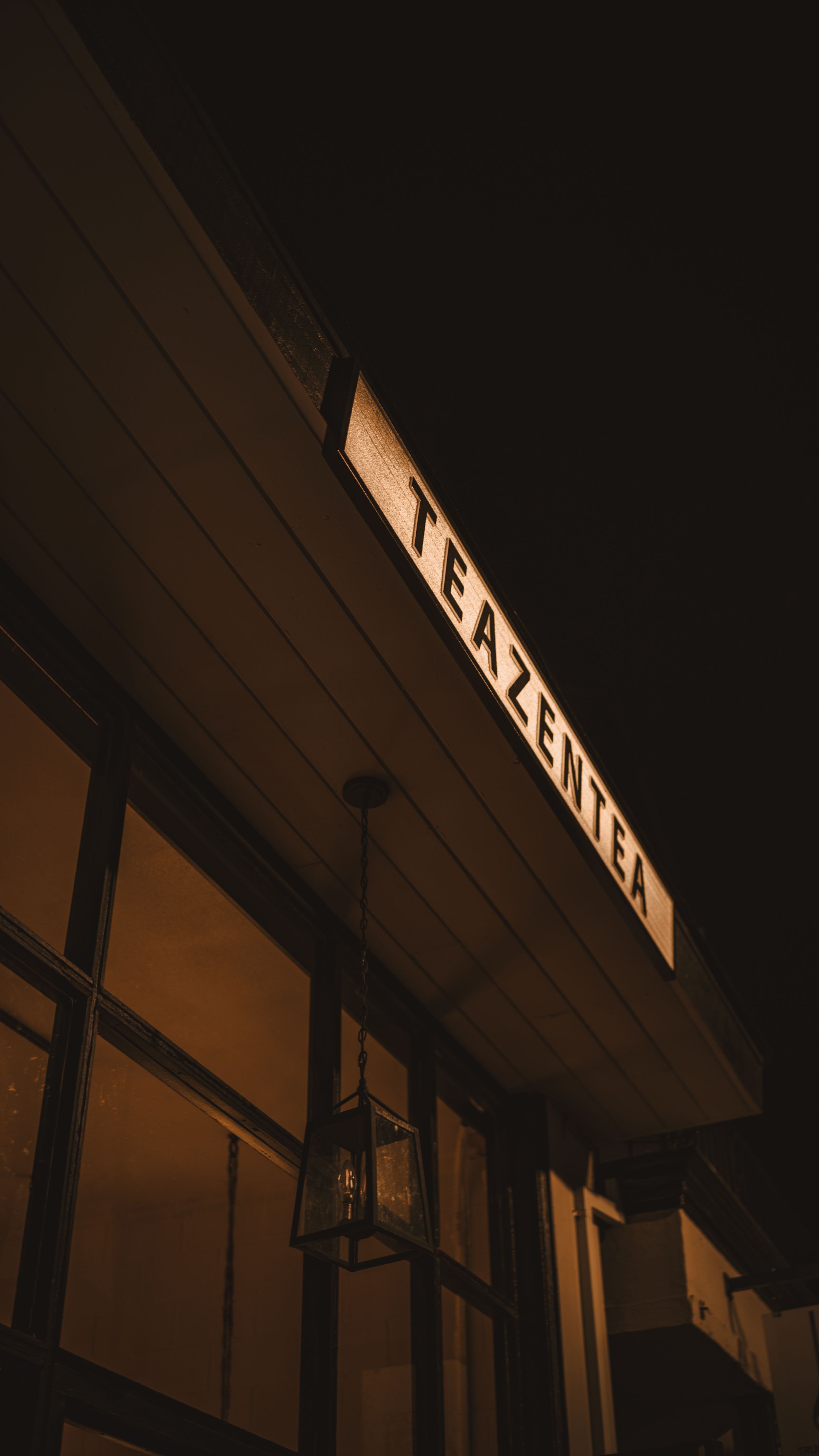 A backlit sign reading 'tea time' illuminated against a dark storefront exterior with glass windows at night.