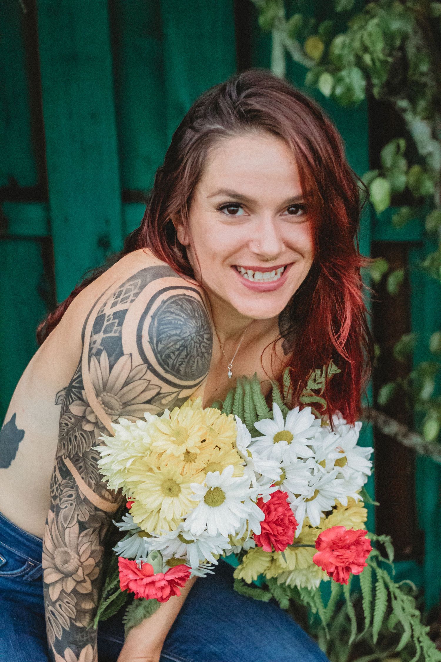 A tattooed woman holding colorful daisies and carnations against a green background.