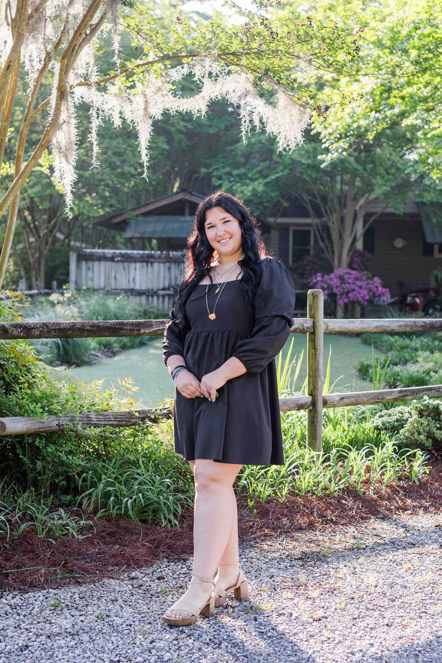 A casual black dress is styled with brown boots and photographed in a garden with wisteria blooms overhead.