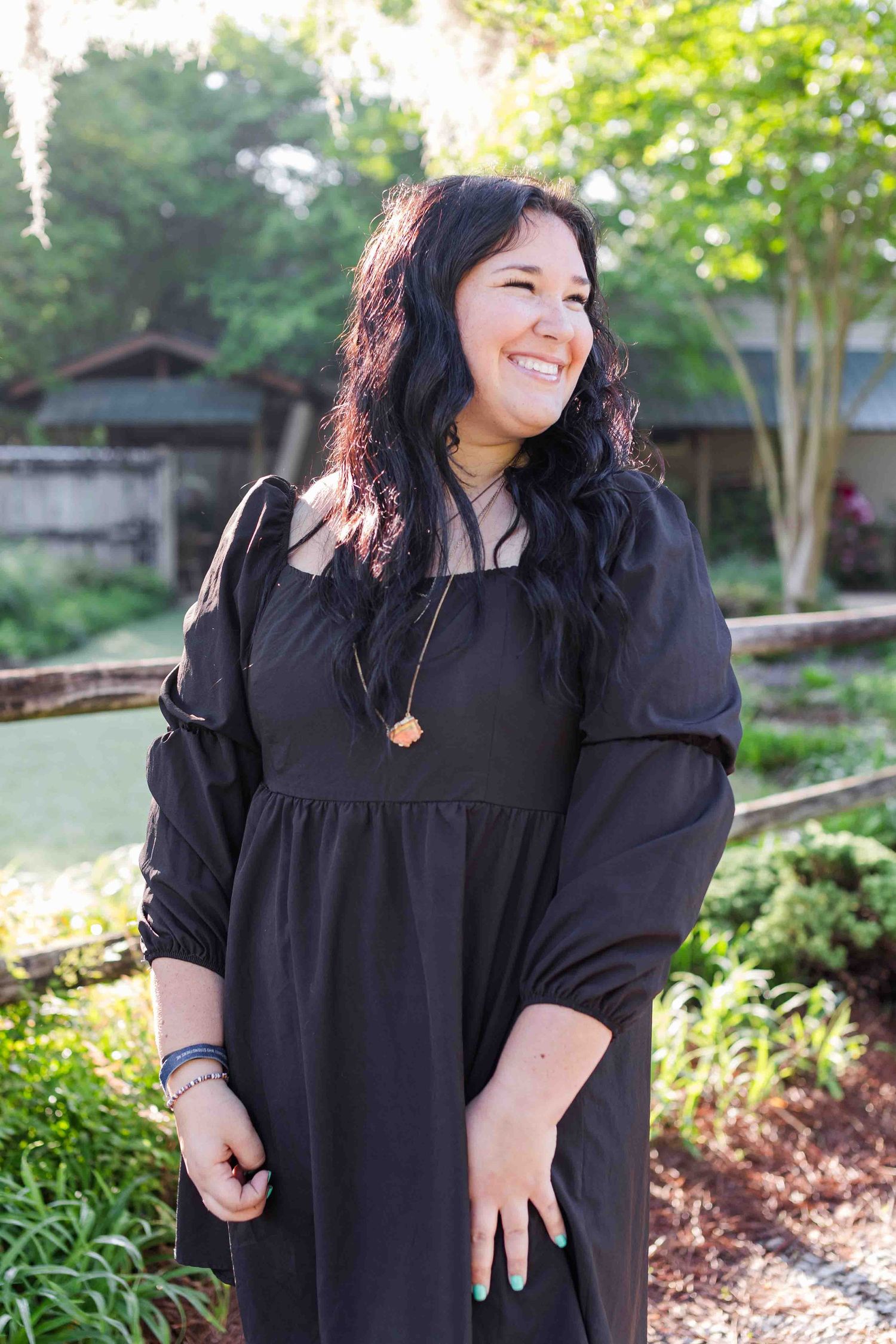 A black long-sleeve dress with empire waist styling is shown outdoors in a garden setting.