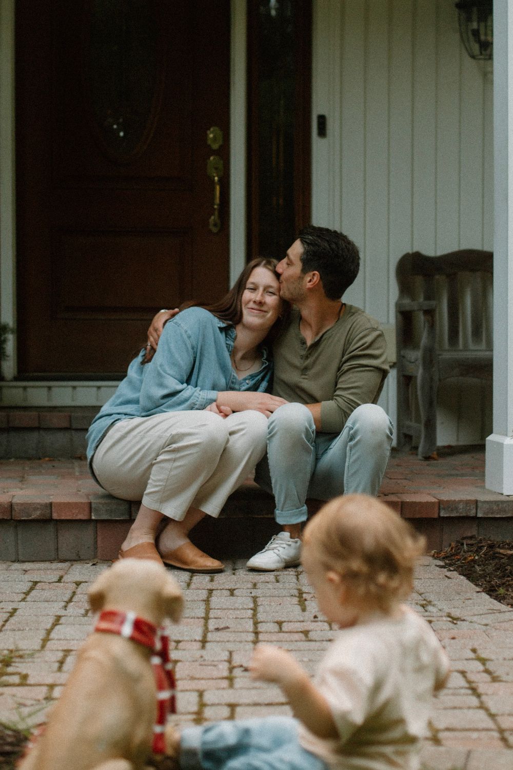 Couple embracing on their front porch while their son looks on during their outdoor family session in West Michigan.