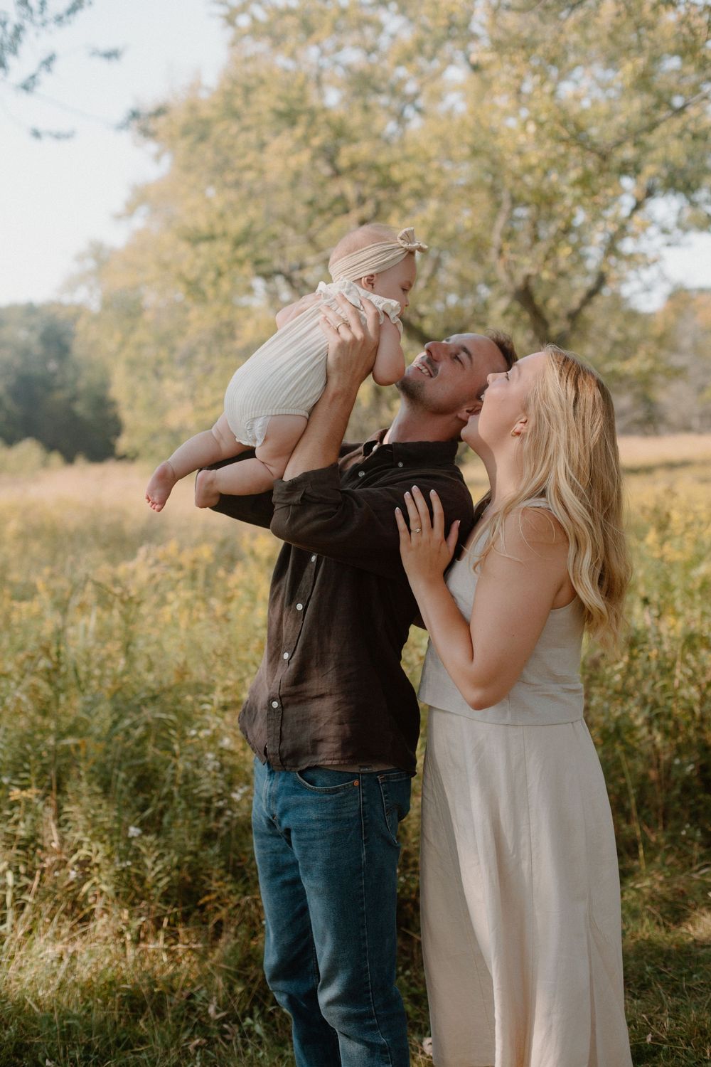 A family of three during their West Michigan family session with their baby in the air and looking down at them.