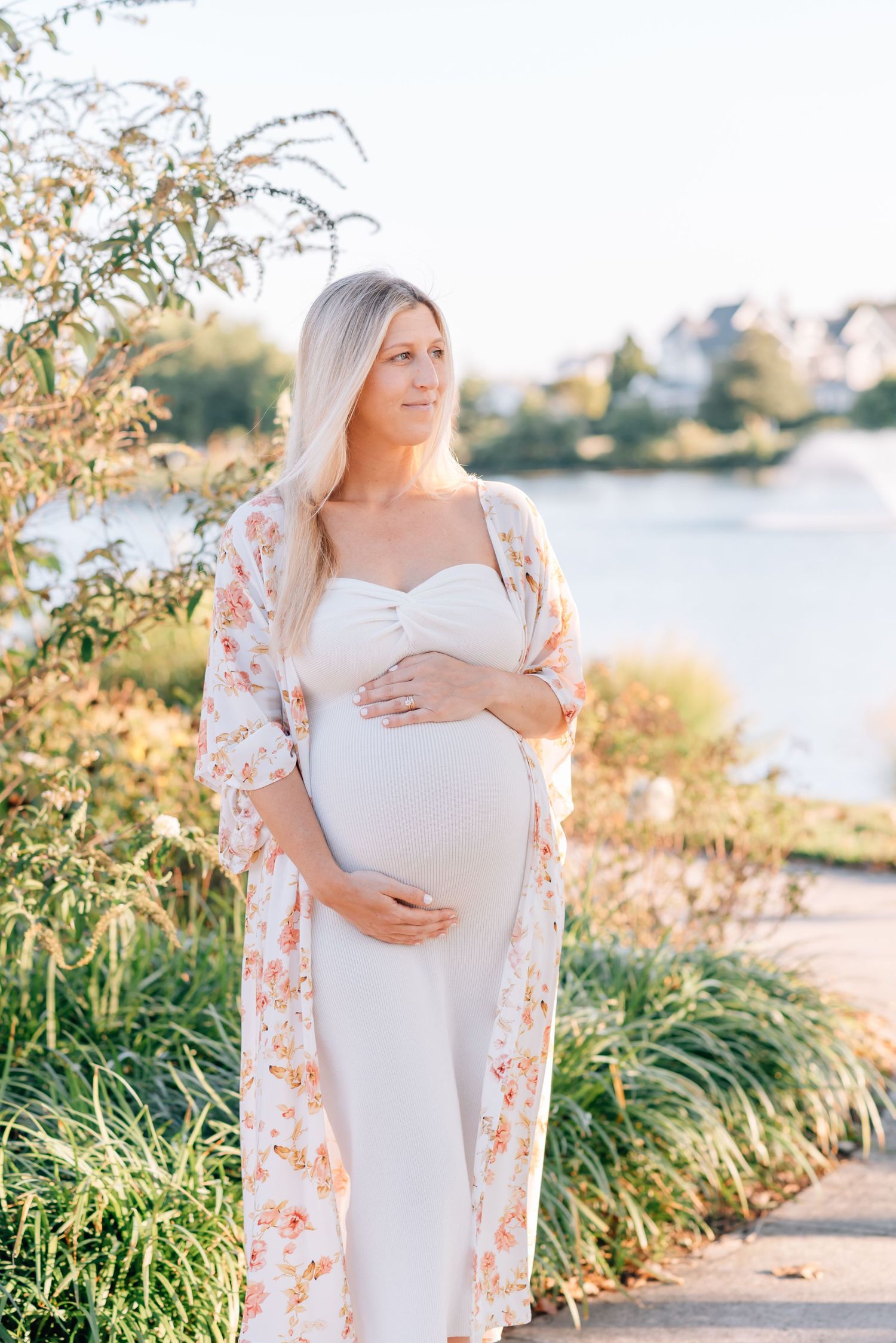 An expecting mother holds her belly looking out into the distance with a lake behind her.