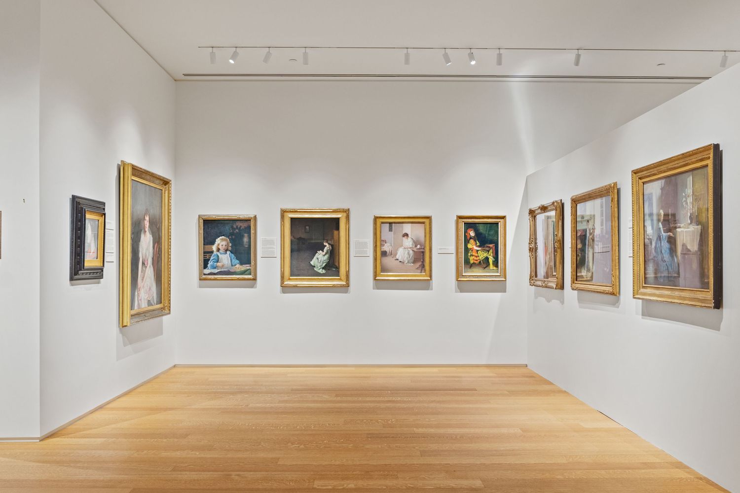 Art gallery hallway with wooden floors and framed paintings displayed on pristine white walls.