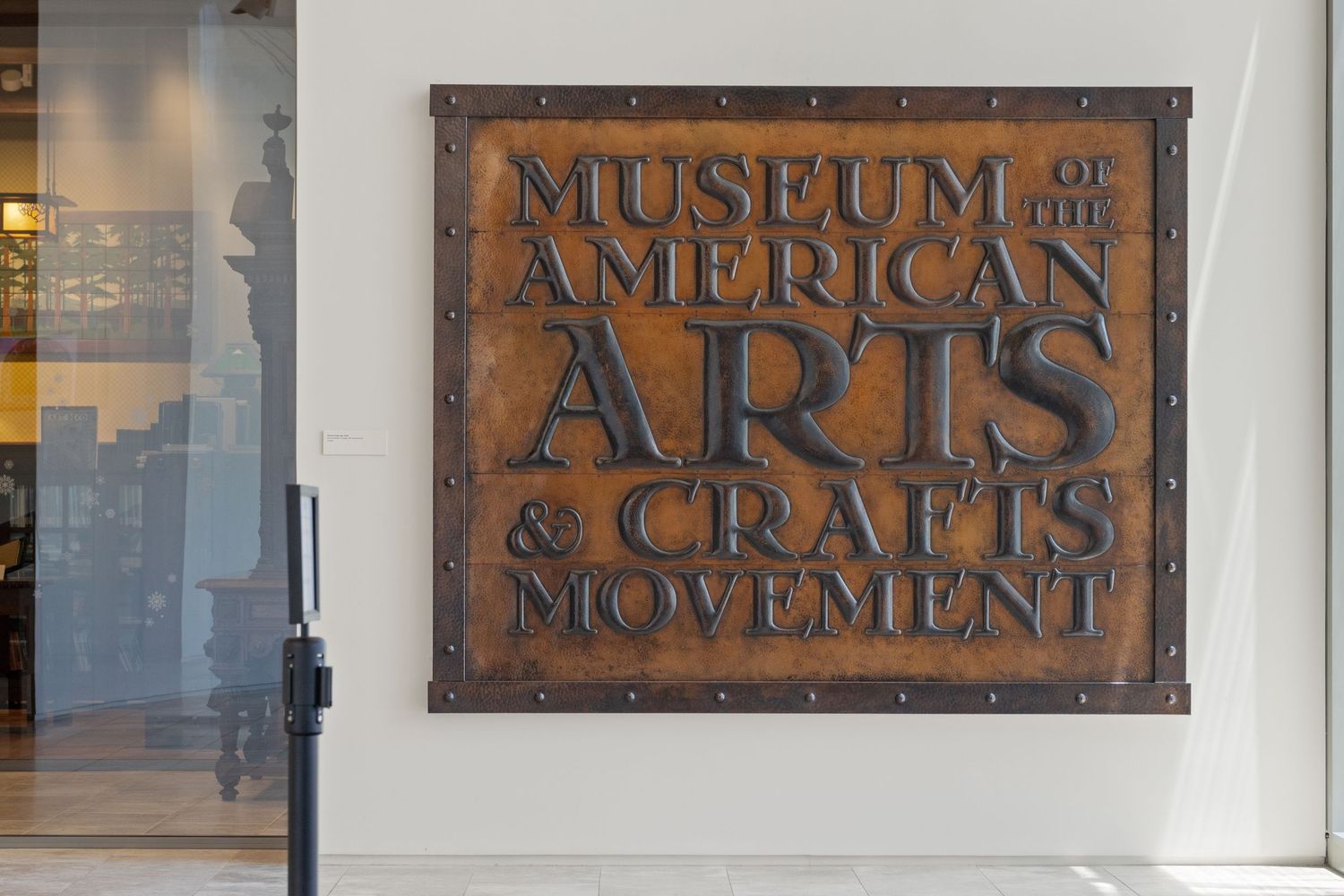 Vintage copper signage reading 'Museum of the American Arts & Crafts' mounted on white wall.