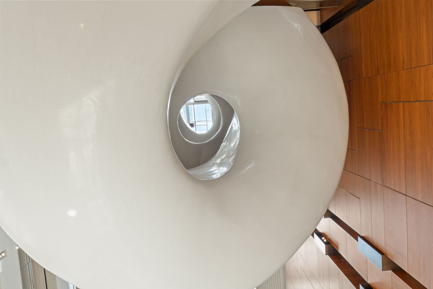 Spiral staircase with white walls and wooden handrails in museum interior.