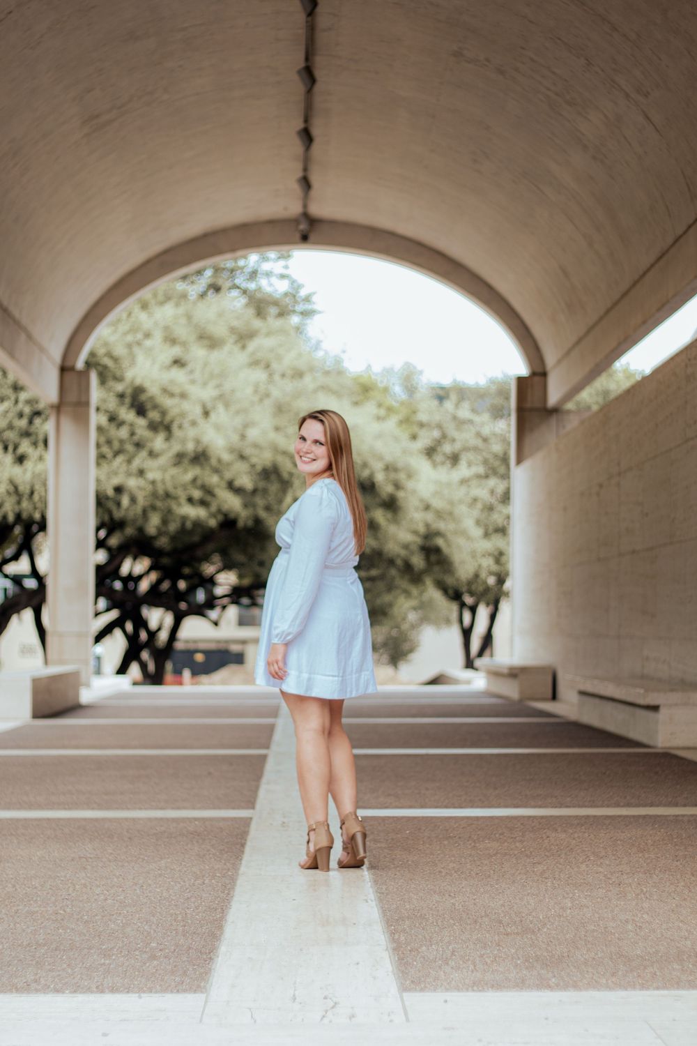 Figure in a light blue dress poses gracefully under an arched passageway with natural lighting and architectural elements.