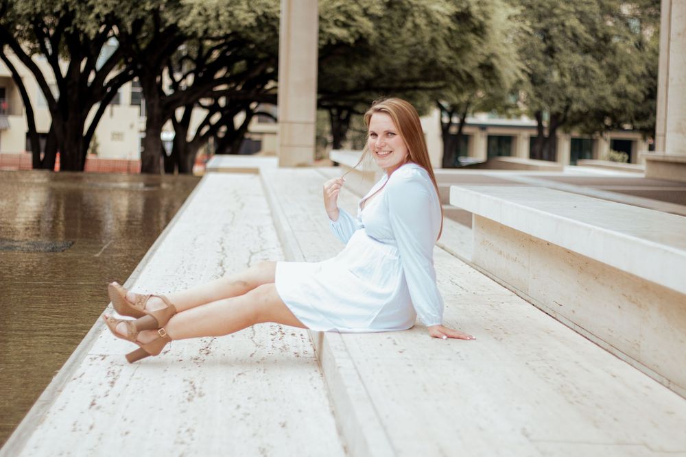 A person in a white dress sits on concrete steps outdoors on a sunny day.