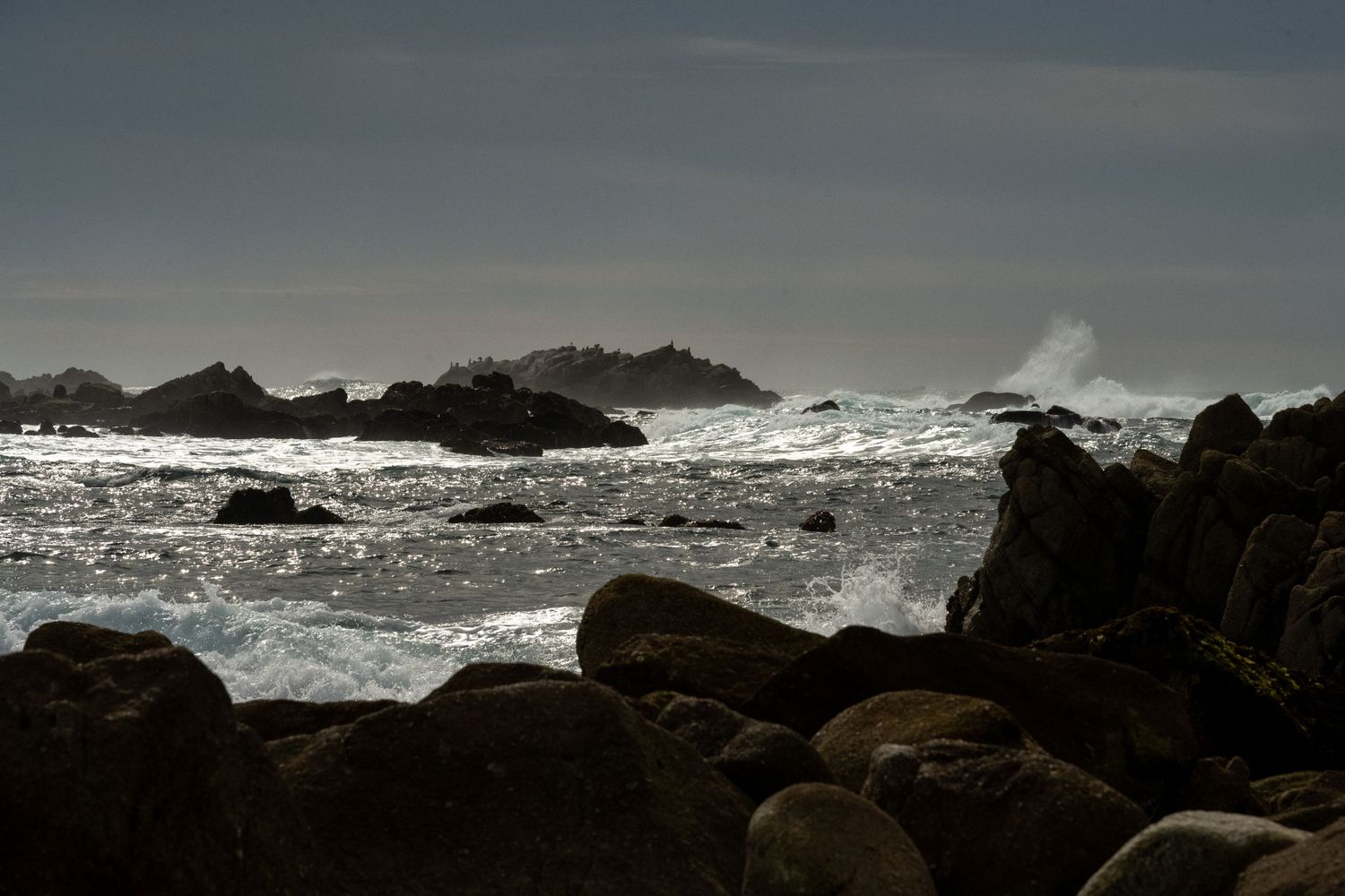 Dramatic seascape with dark rocks and crashing waves against rocky shoreline.