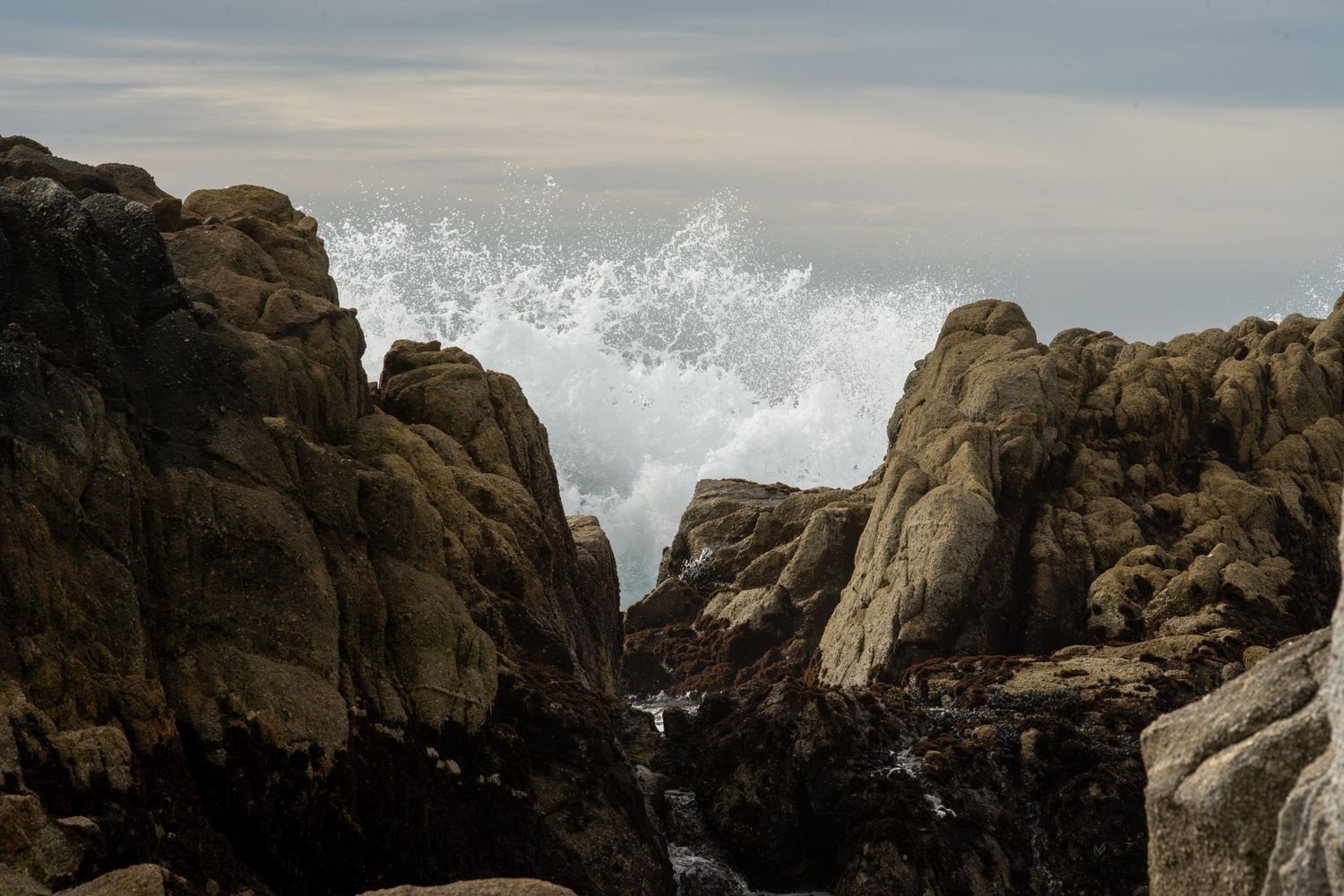 Dramatic ocean waves crash against large coastal rocks creating white spray.