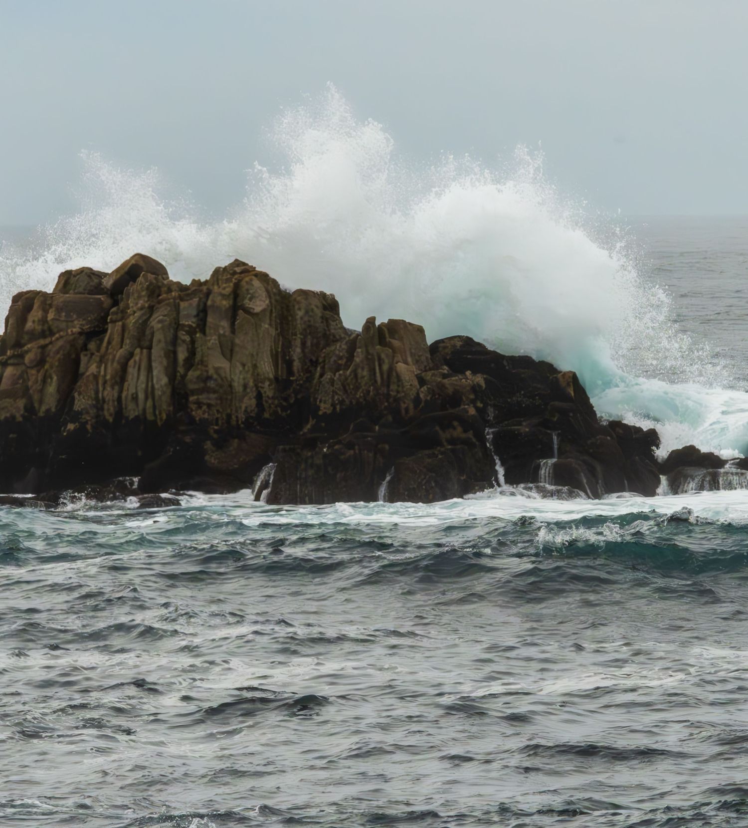 Large ocean wave crashes against rocky cliff face creating dramatic splash.