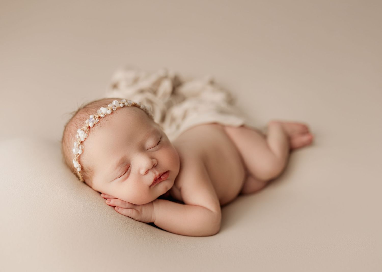 Peaceful sleeping newborn baby lying on beige backdrop wearing delicate pearl headband. Southeast Michigan Newborn Studio Photographer