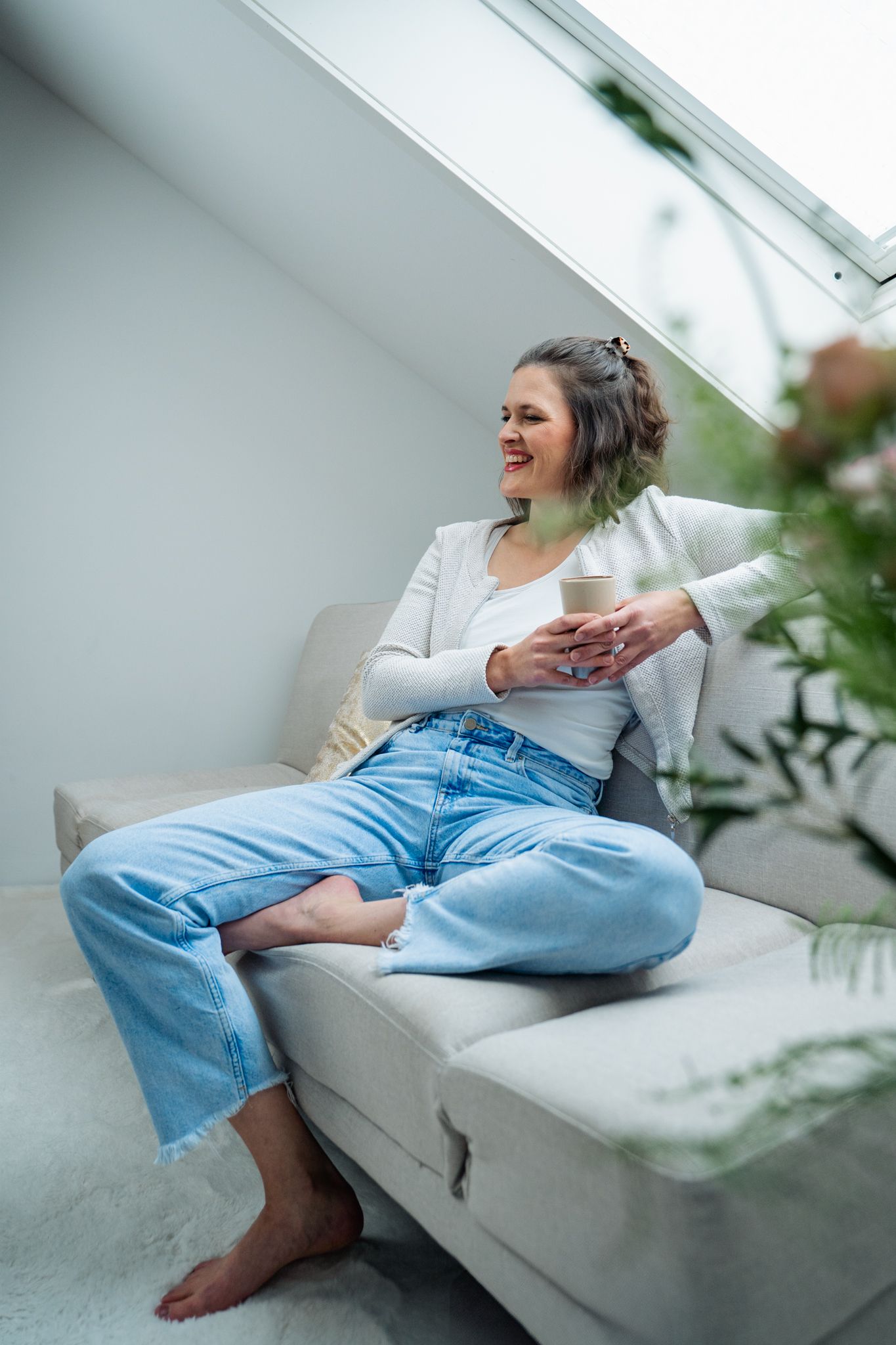 Relaxed lifestyle scene of person lounging on white couch in bright sunlit room.
