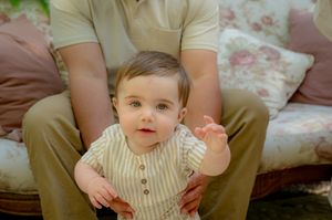Baby in cream-colored outfit sitting on floral patterned couch cushions.