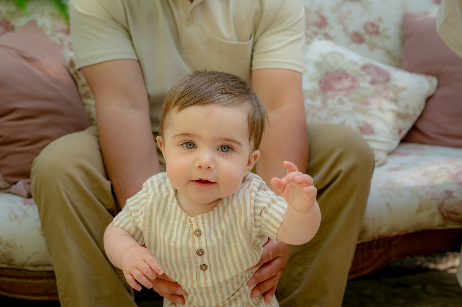 Close-up view of hands holding a small baby wearing a striped onesie on a soft white blanket.