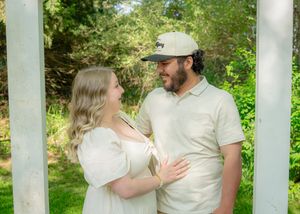 Outdoor family portrait with white columns and lush garden backdrop in natural lighting.