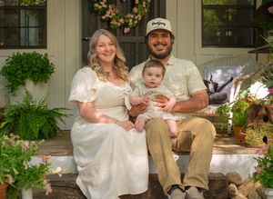 Wide shot of family seated on front porch steps with classic farmhouse architecture.