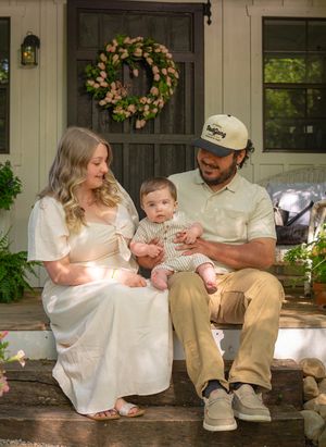 Family relaxing on a rustic front porch with decorative wreaths and plants.