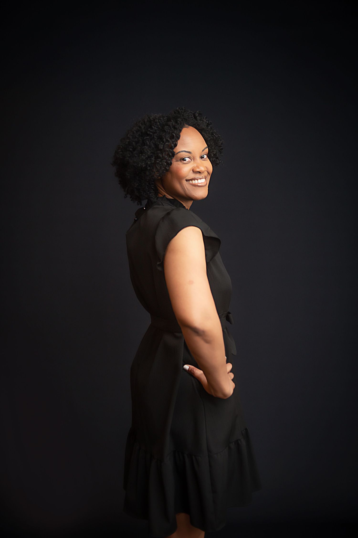 Professional portrait of a woman in a black dress posing against a dark background.