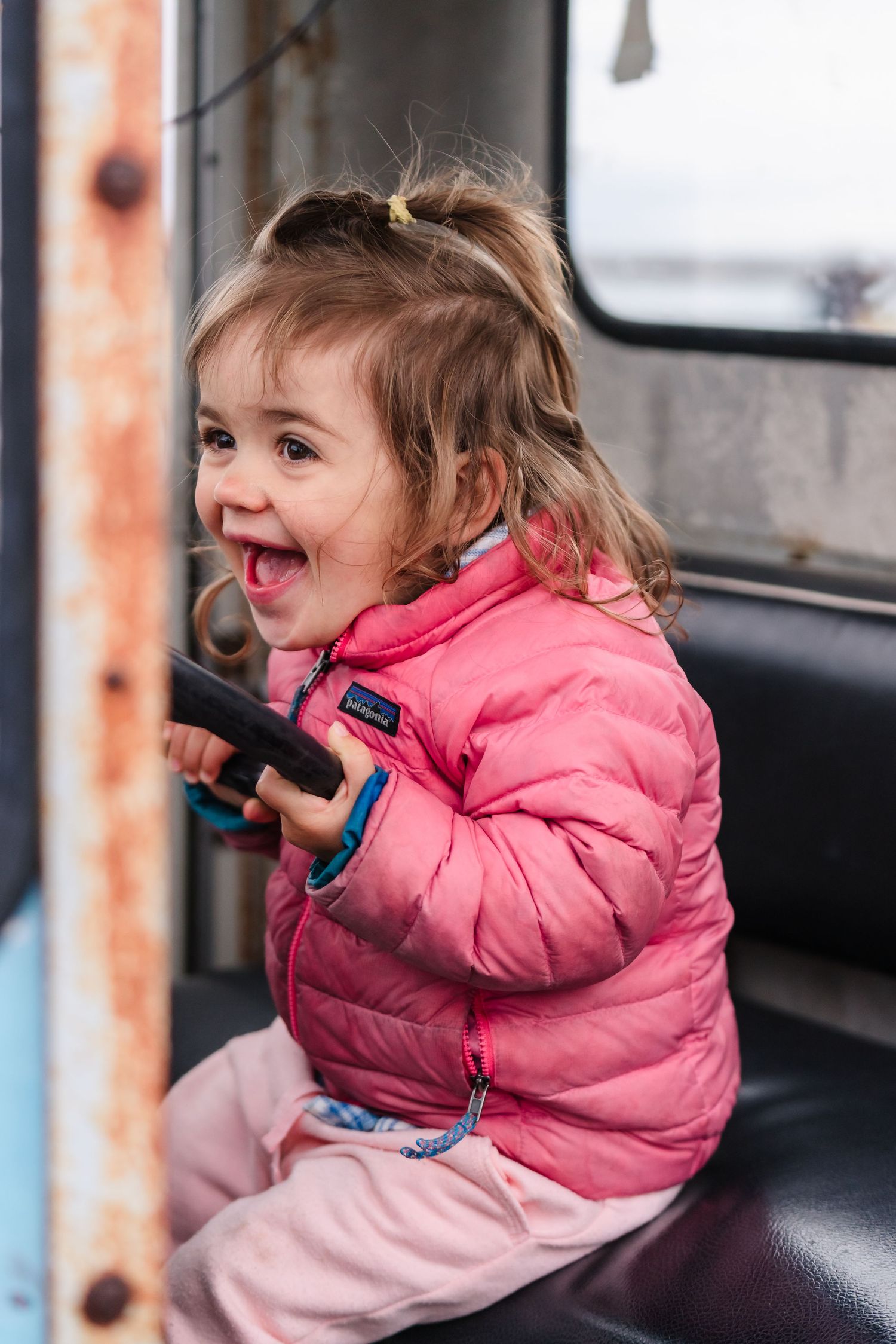 Small child in pink winter coat sitting in dark vehicle and talking on handheld radio. Located on the Santa Cruz Wharf, California.