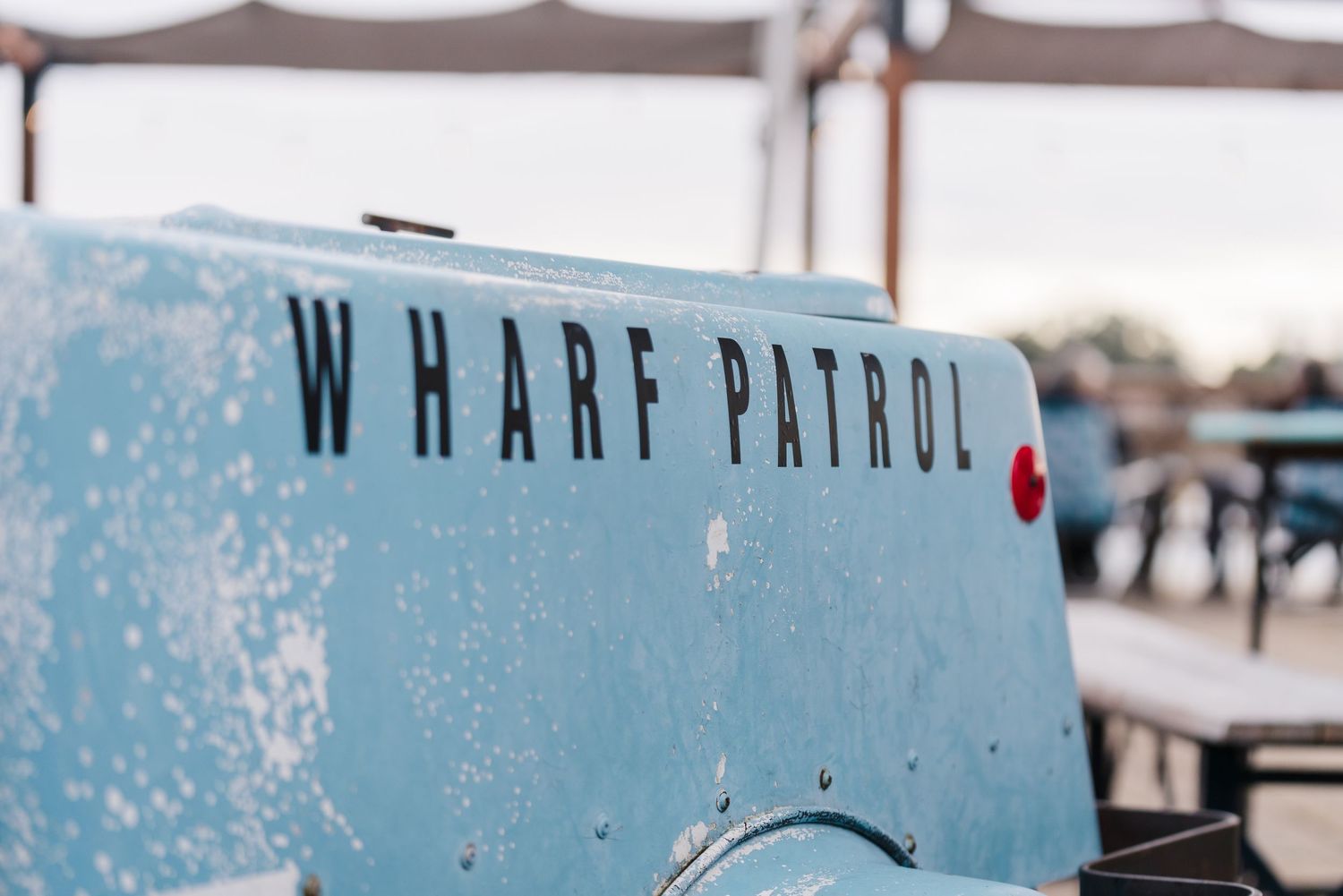 Light blue boat hull with 'WHARF PATROL' text displayed against a blurred nautical background. Located on the Santa Cruz Wharf, California.
