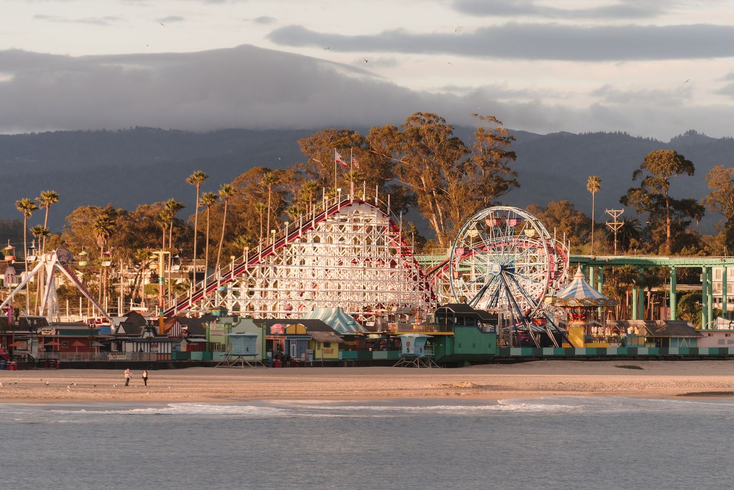Vintage amusement park rides and roller coaster illuminated at sunset along the Santa Cruz Beach Boardwalk in California.
