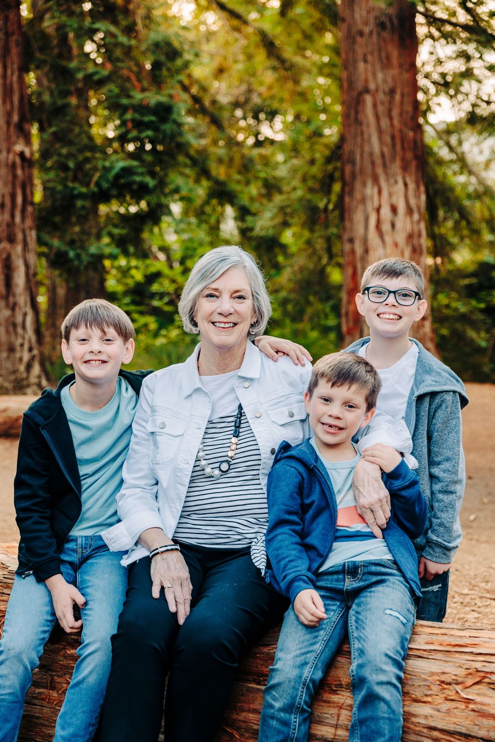 A playful family photo session in a wooded park with everyone sitting on a fallen log wearing coordinating blue outfits.