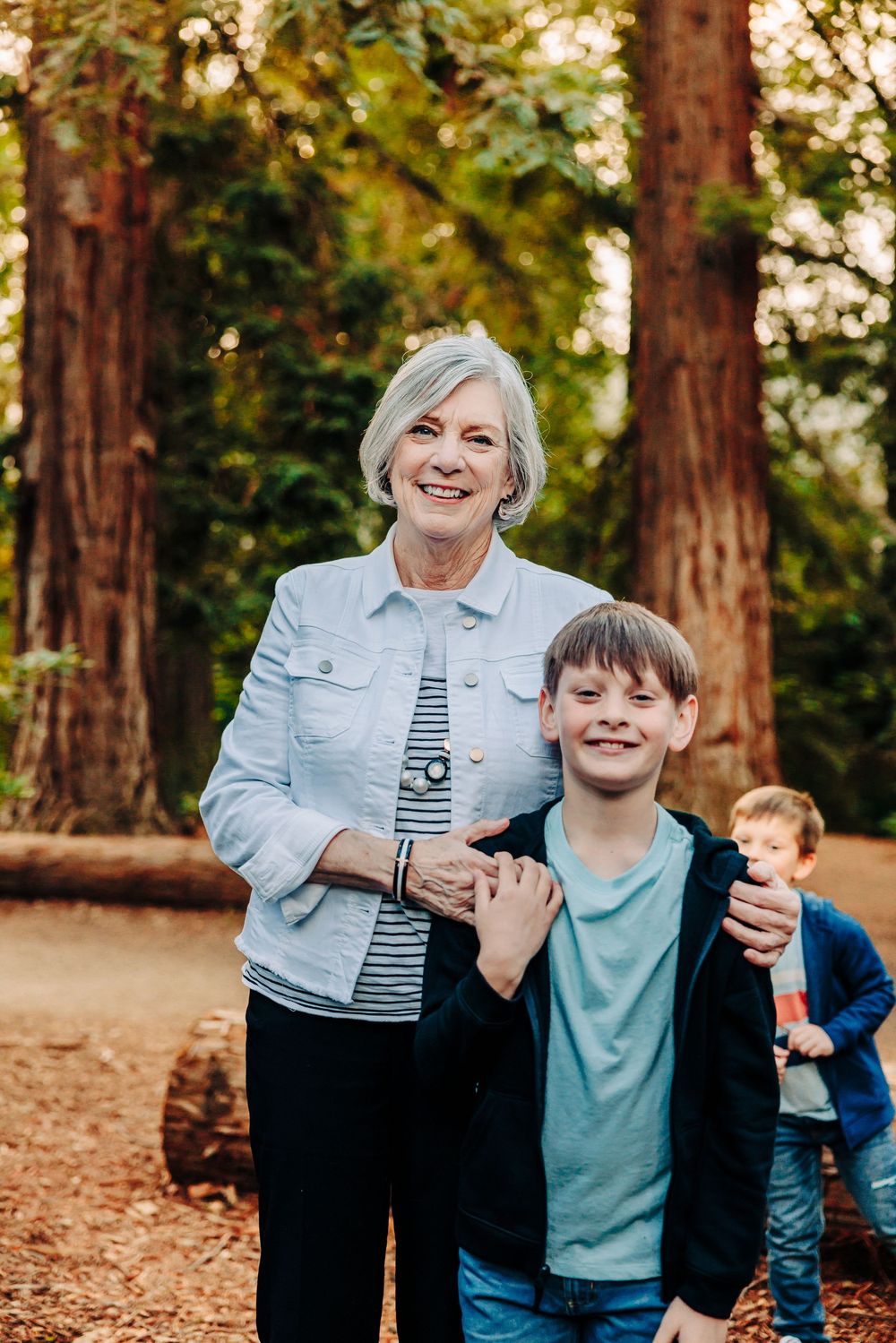 Family enjoying playful moments together in a sunlit forest with tall redwood trees in the background.