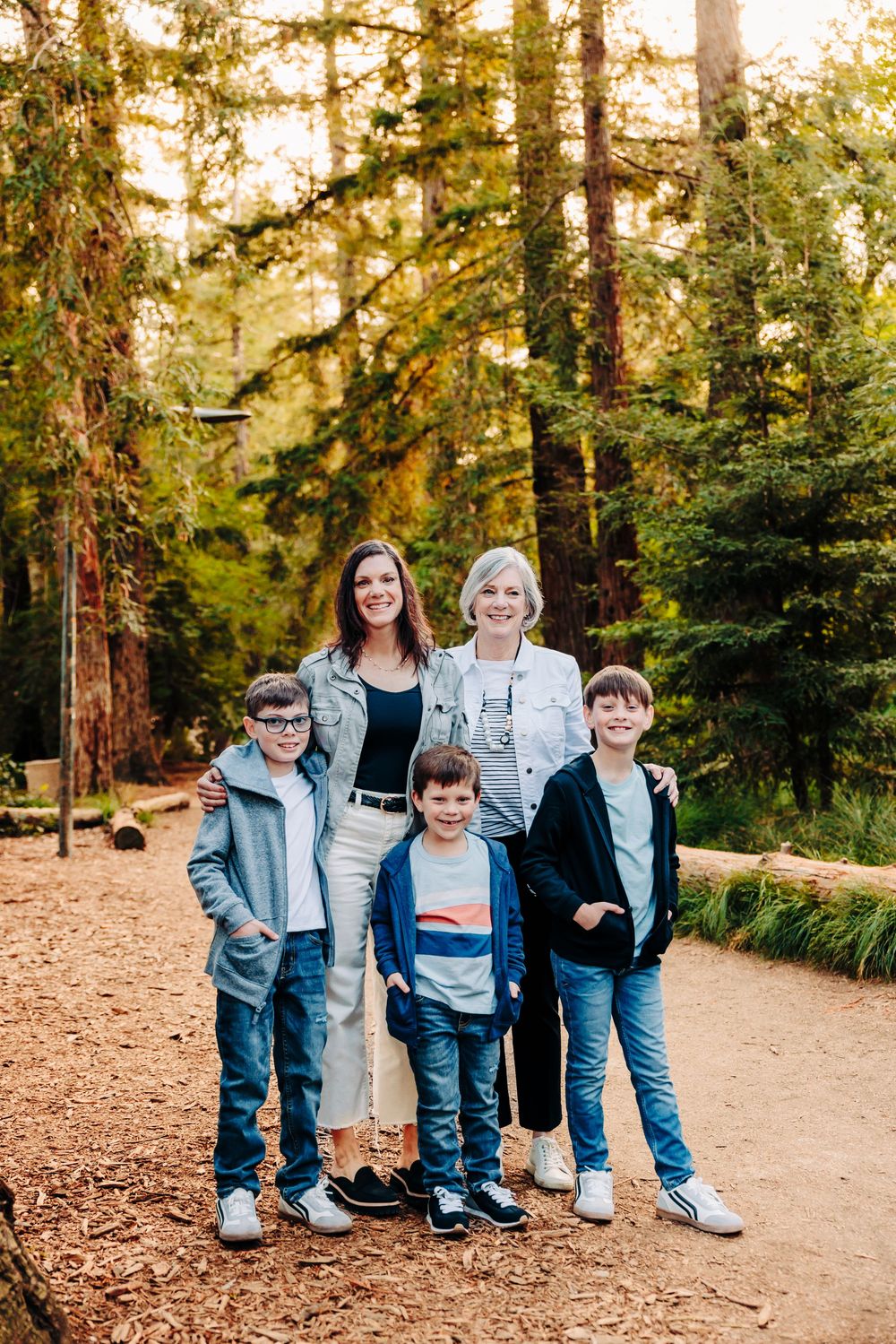 A casual outdoor family photoshoot in a sunlit forest with people wearing coordinated denim and casual attire.