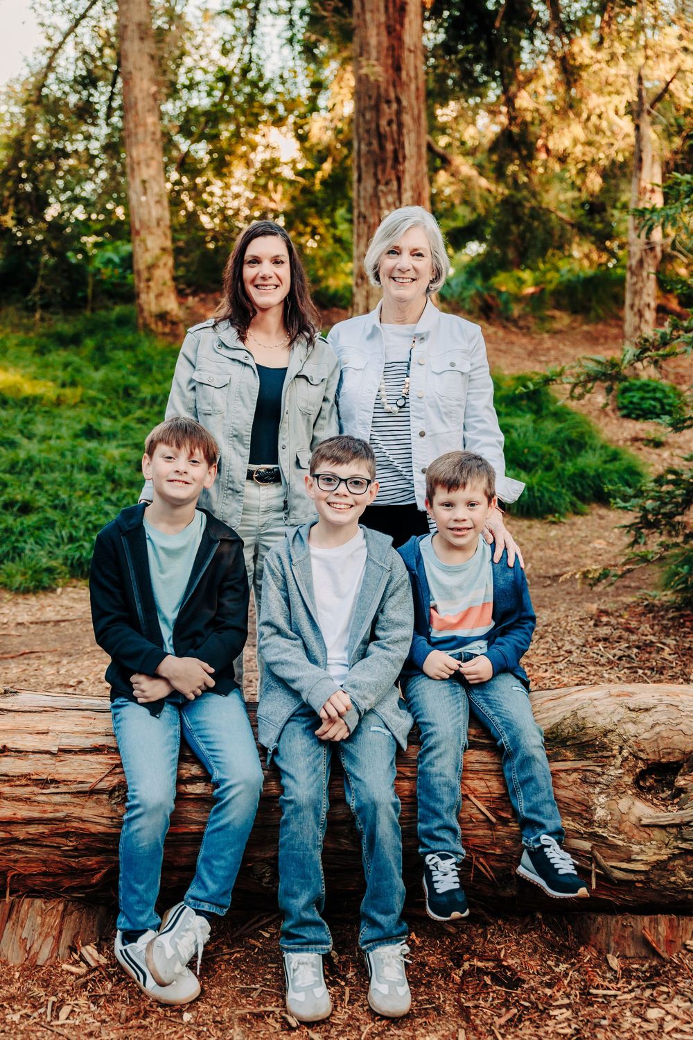 A group sits together on a fallen log in a sunlit forest during a casual outdoor photo session.