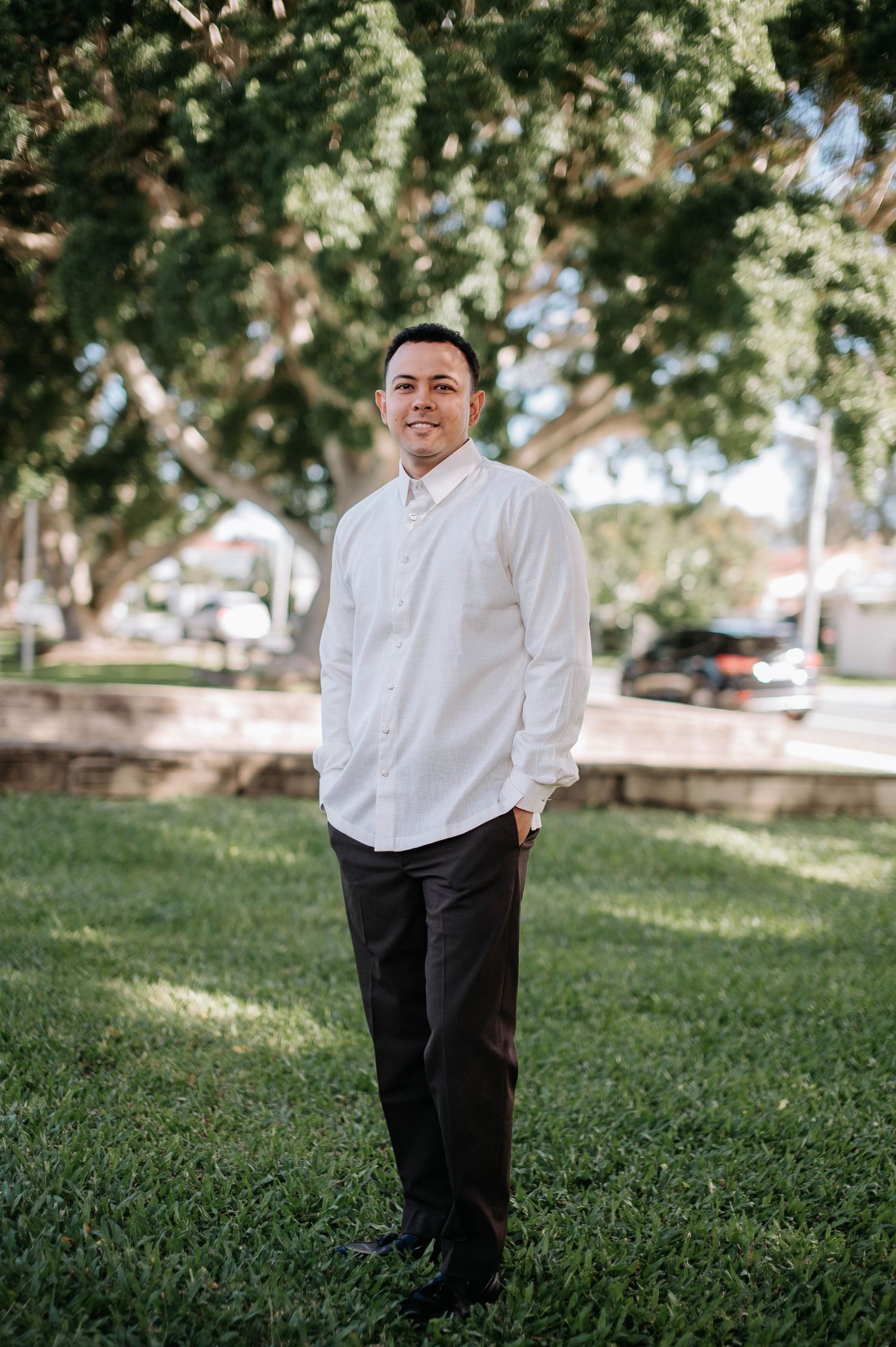 Person standing on grass in front of trees wearing a white button-up shirt and black pants in a casual outdoor setting.