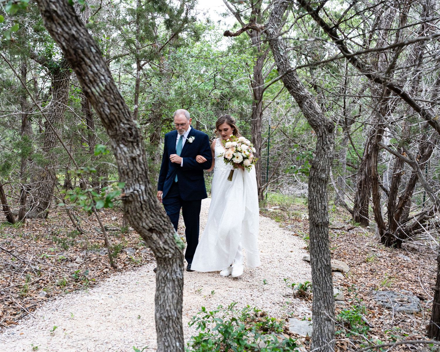 Wedding photo of bride and father walking through the woods