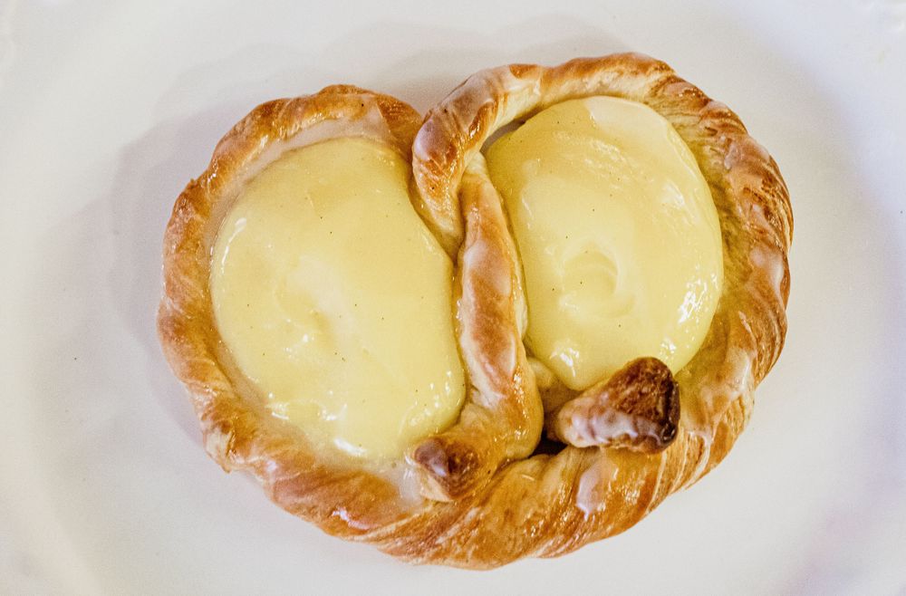 A heart-shaped Danish pastry filled with golden custard cream on a white plate.