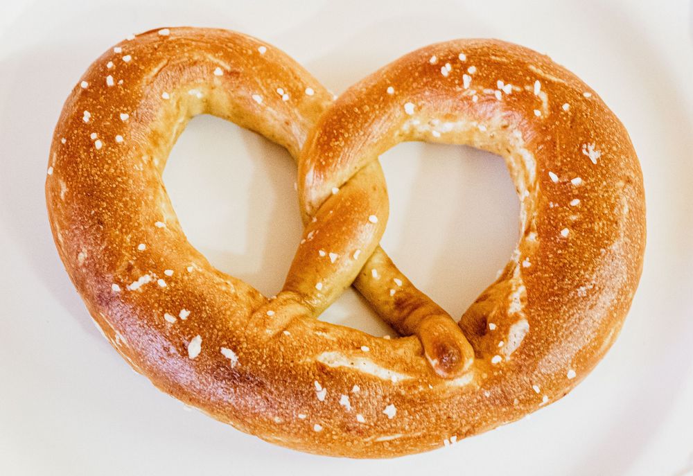 A freshly baked soft pretzel with coarse salt sprinkled on its golden-brown surface.