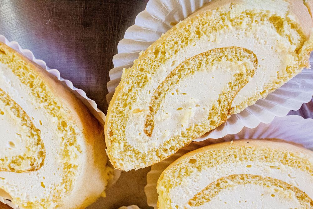 Close-up view of sliced yellow sponge cake roll with creamy white filling on paper liners.