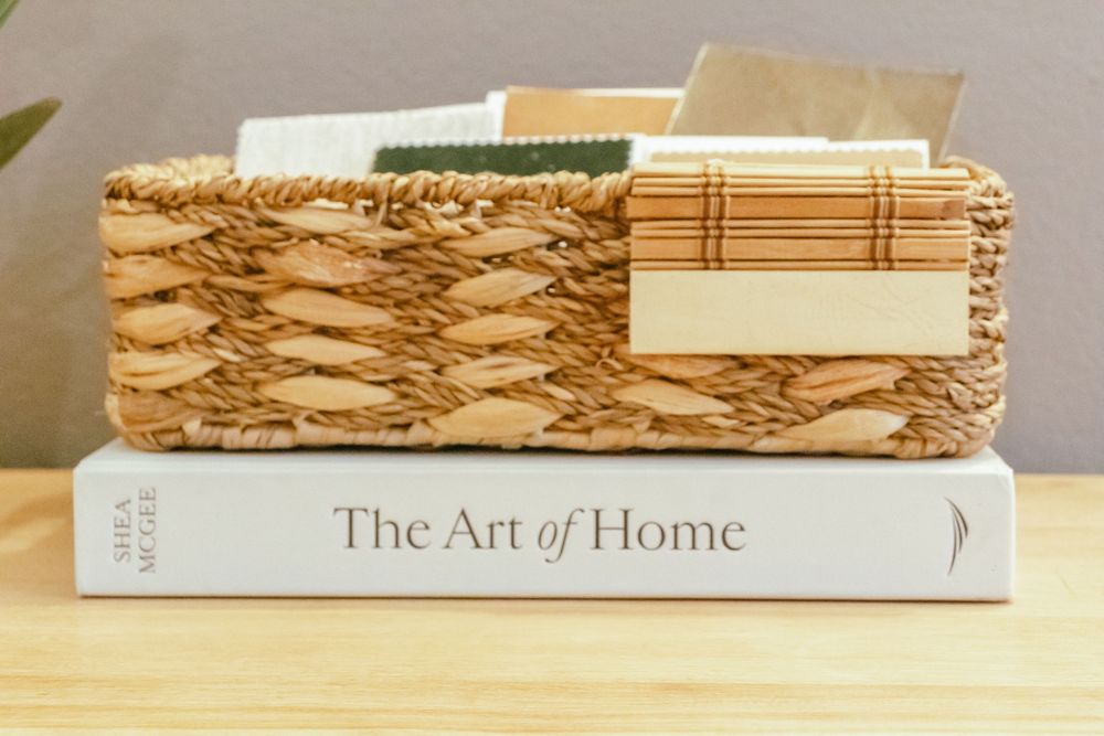 Woven basket and bamboo placemat sitting on top of 'The Art of Home' book on wooden surface.