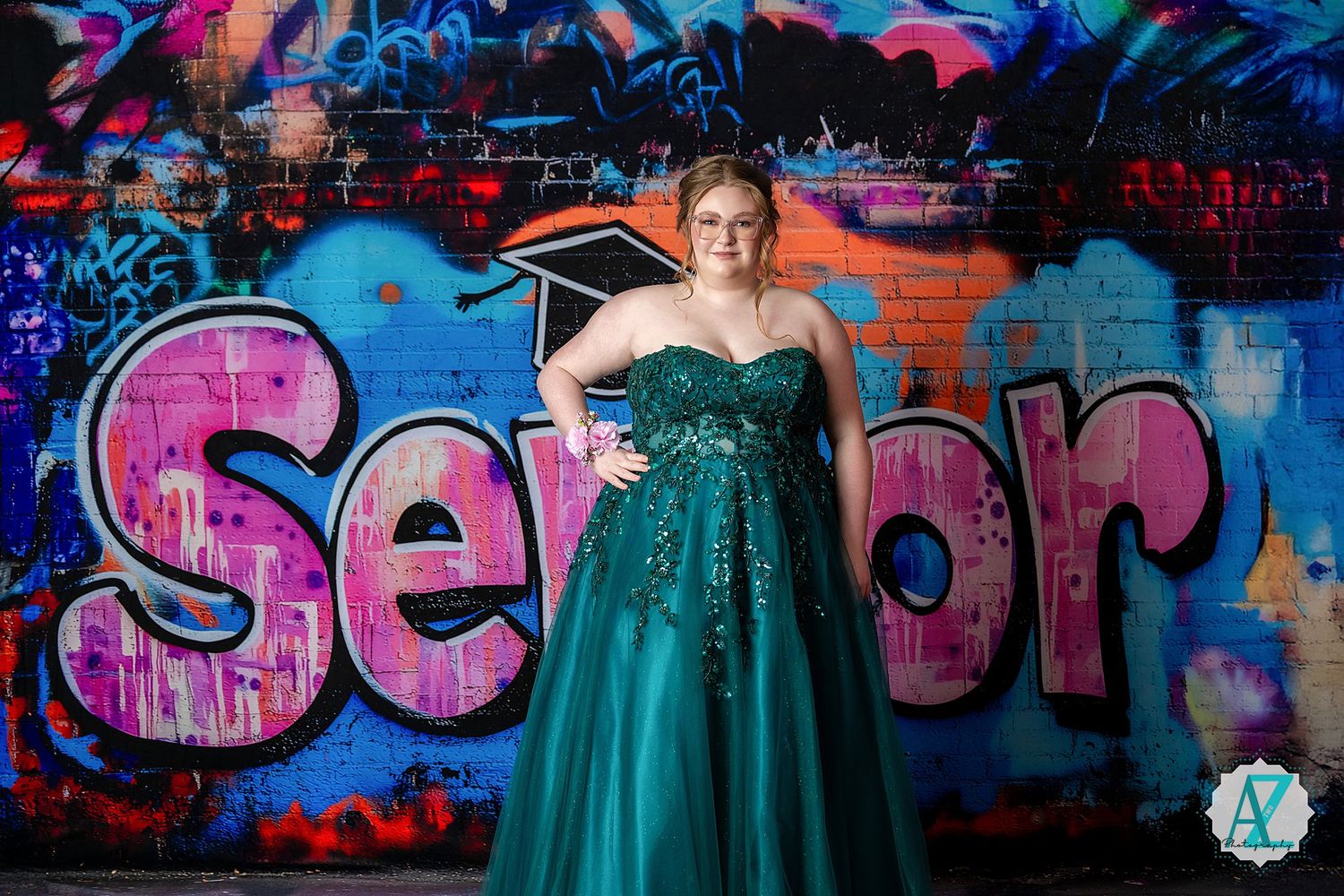 A emerald green prom gown is photographed against a vibrant graffiti wall with pink lettering.