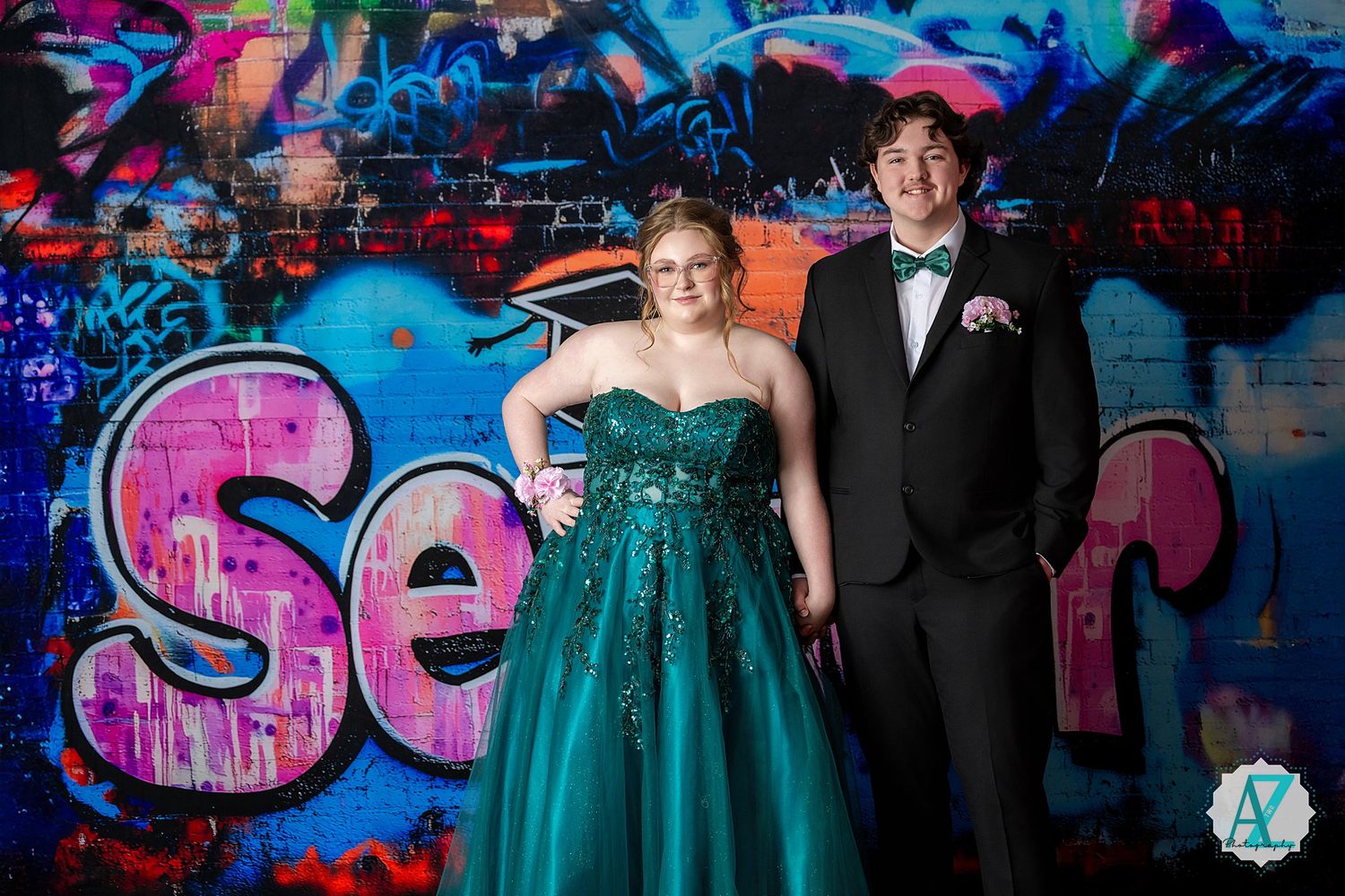 Formal couple poses in front of vibrant graffiti wall with person wearing emerald green sequined gown.
